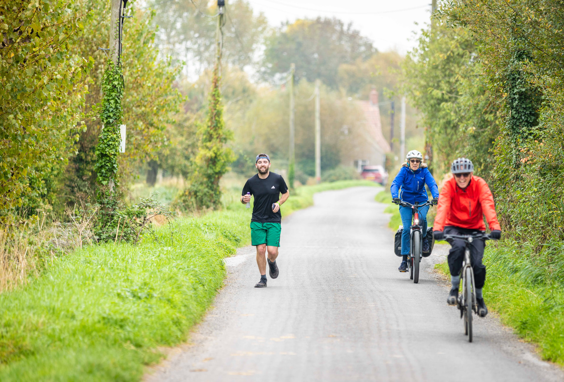 A runner and two cyclists on a country lane on the route